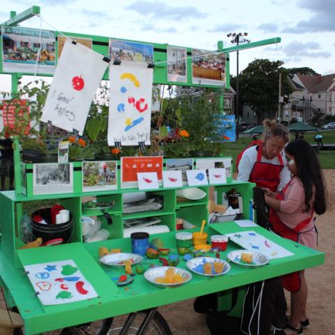 Laura Baring-Gould stands next to her mobile art cart. A young girl investigates the contents.