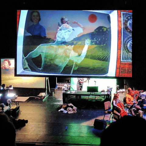 Puppeteers and an orchestra are on either side of a projection of a TV that shows a character running.