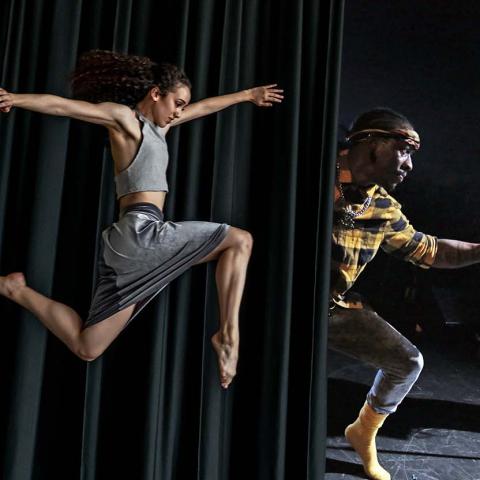 A dancer leaps before a curtrain. Behind the curtain, the a guitarist and dancer.
