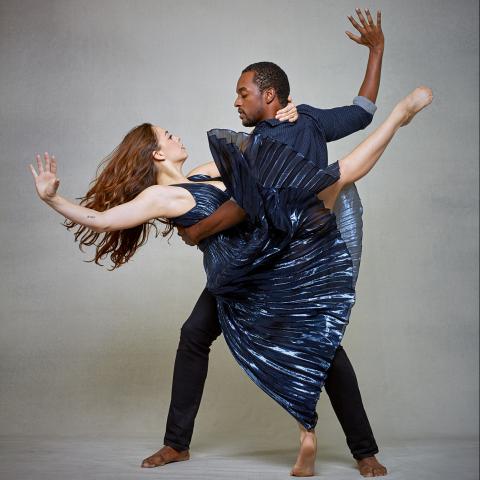 A man and woman dance in front of a gray backdrop.