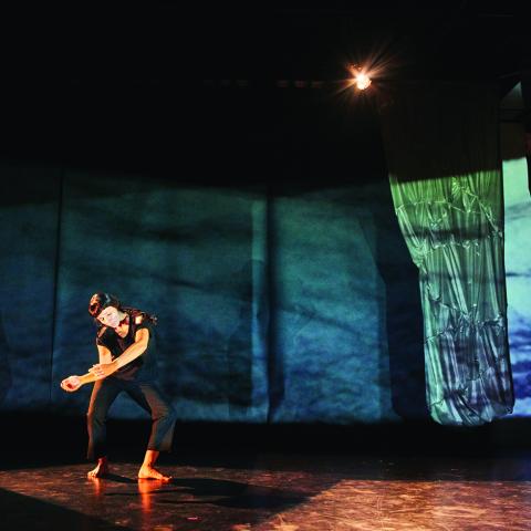 Woman in black dances in front of a blue and green projection of a texture.
