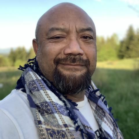 Bronze bald man with a smirk wearing a blue and white keffiyeh aka hatta.