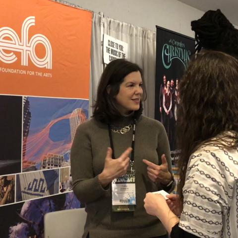 Image: Cathy Edwards speaks to attendees at APAP 2018. NEFA's orange banner is in the background.