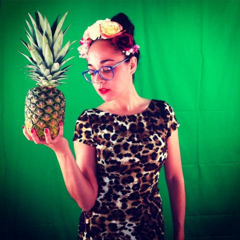 Paloma poses in front of a green backdrop with a pineapple in her hand.