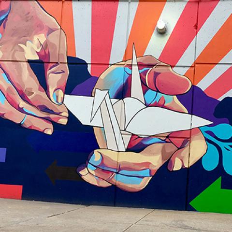 A mural of two hands holding an origami swan, with rays of red and orange sunsetting behind.