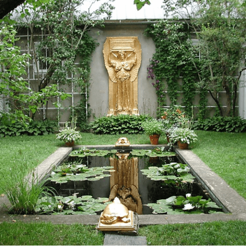 An atrium with a water pond, golden statues, and trees.