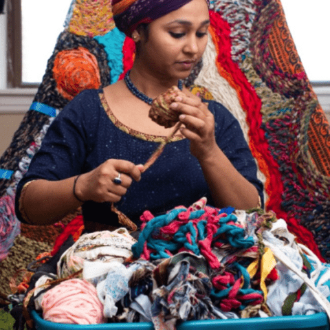 A brown woman rolls a basket of yarn.