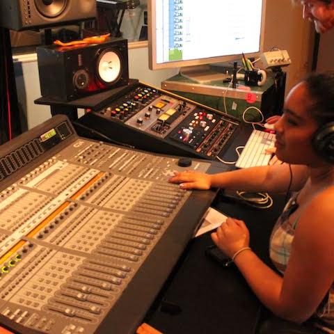 A few sound engineers are seated in a recording booth in front of a complex looking soundboard
