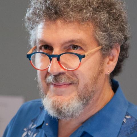 A man with curly hair and a beard wearing a blue shirt and colorful round glasses