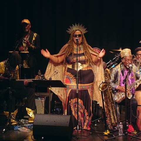 Black folks wear Afro-futurist inspired outfits and play jazz instruments.